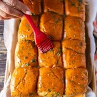 A hand brushing the bread tops with the garlic herb butter