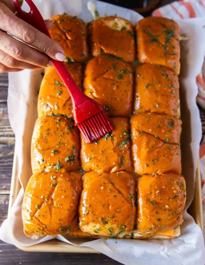 A hand brushing the bread tops with the garlic herb butter