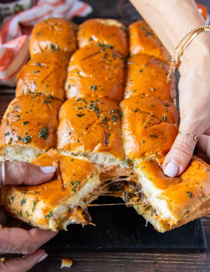 Cheese burger sliders our of the oven and hands stretching them apart showing the cheesy melt