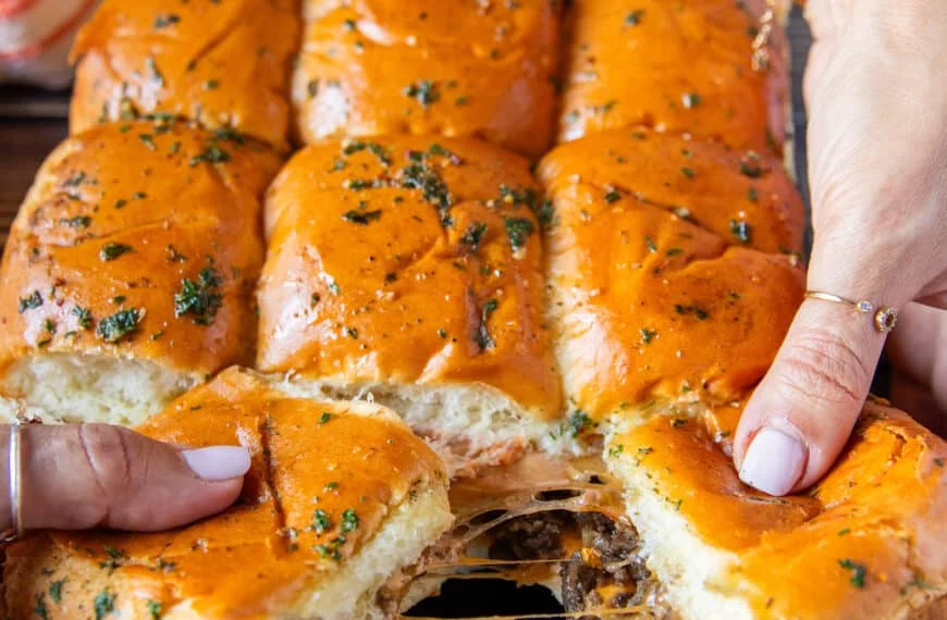 Cheese burger sliders our of the oven and hands stretching them apart showing the cheesy melt