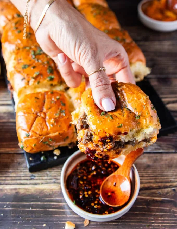 A hand holding one slider and dipping it into a sauce to eat