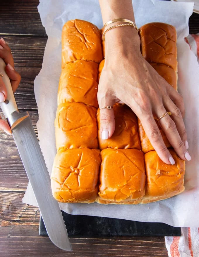 A hand using a serrated knife to cut the slider bread in half