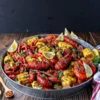 close up of a crawfish boil with crawfish , corn, potatoes, sausage, green beans and lemon wedges on a large platter ined with newspaper