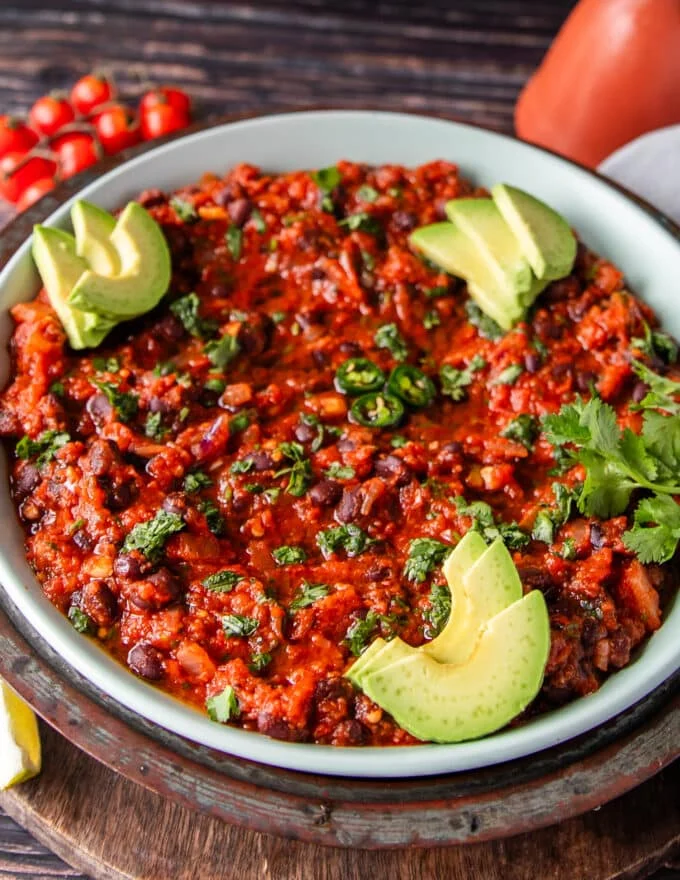 close up of Mexican black beans plate topped wtih avocado slices, cilantro and jalapeños