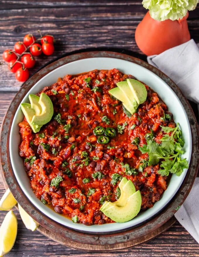 Mexican Black beans on a plate garnished with avocados, cilantro and lots of lime