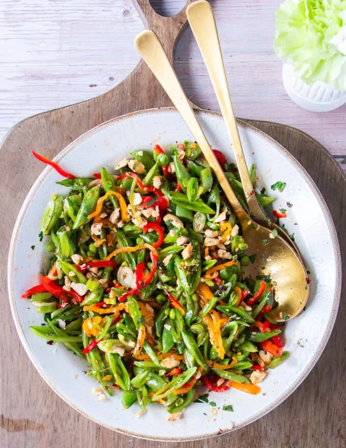 Snap pea salad on a plate with snap peas, carrots, peppers, cilantro, green onions and some crunchy nuts on top