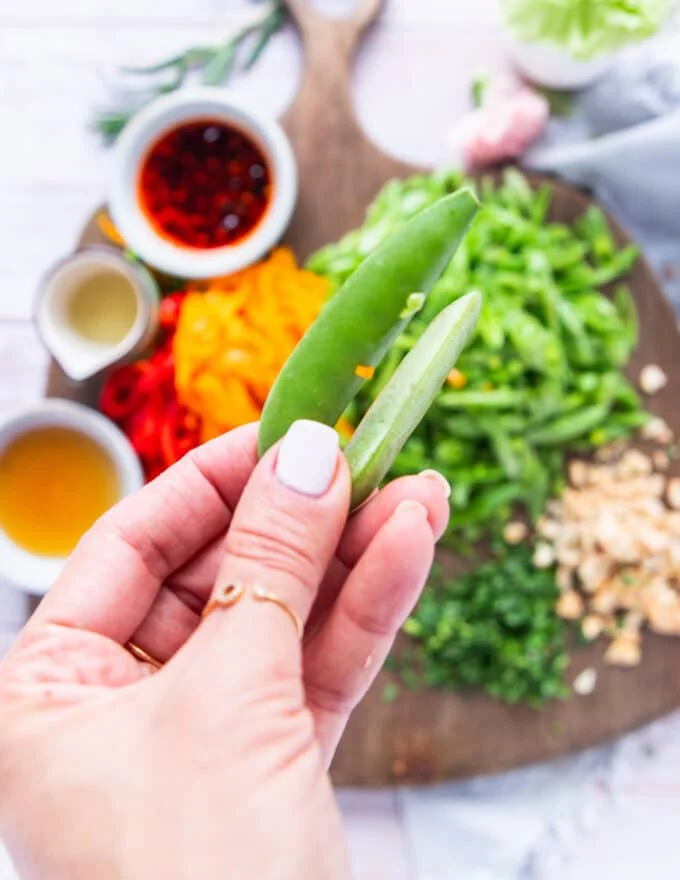 A hand holding fresh snap peas close up starting to prepare the snap pea salad