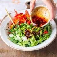 A hand pouring the salad dressing over the salad ingredients bowl and ready to get everything tossed well