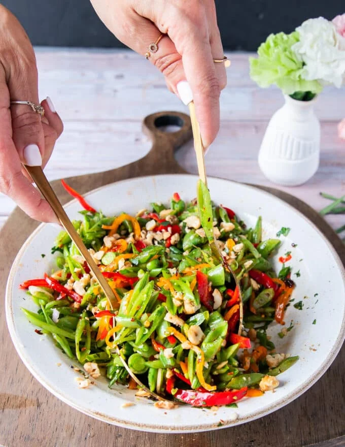 Snap pea salad being tossed well together using salad spoons