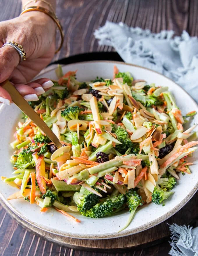 A hand using a fork to spoon in some crunchy broccoli slaw