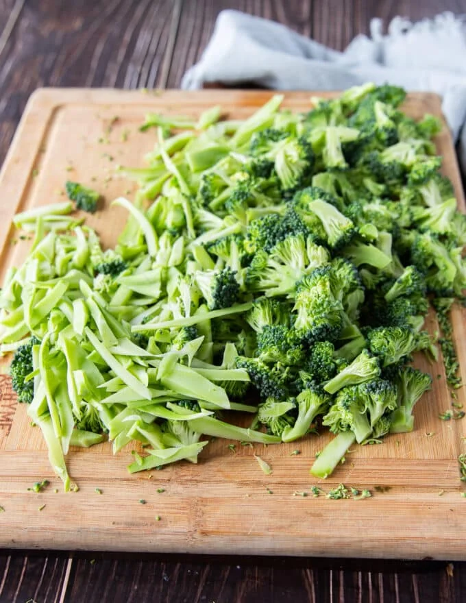 Broccoli stalks and florets are shredded thinly on a wooden board ready to make broccoli slaw
