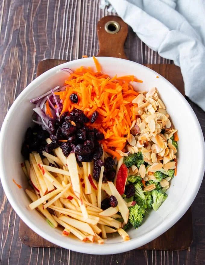 remaining veggies like carrots, apples and onions along with toasted nuts, cranberries and broccoli are all added to a bowl