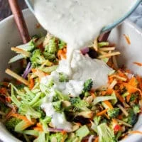 Dressing being poured over the bowl of broccoli slaw ingredients