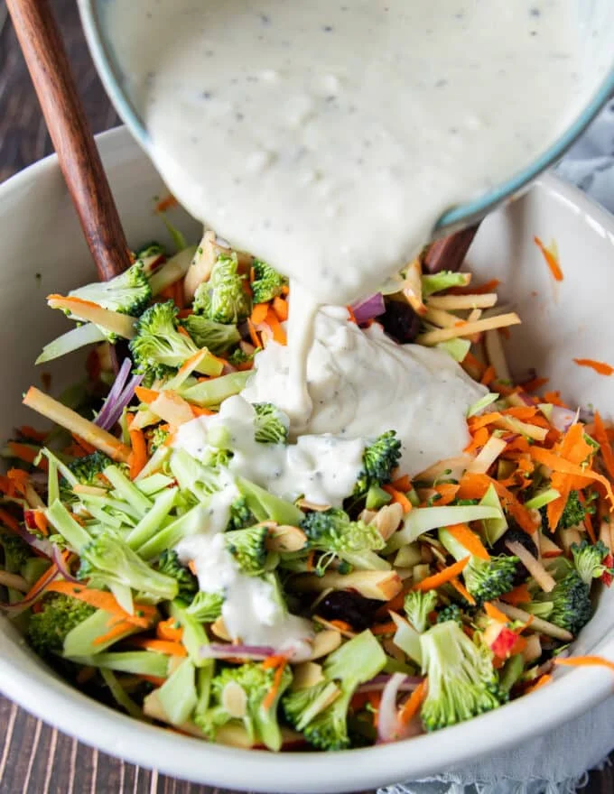 Dressing being poured over the bowl of broccoli slaw ingredients