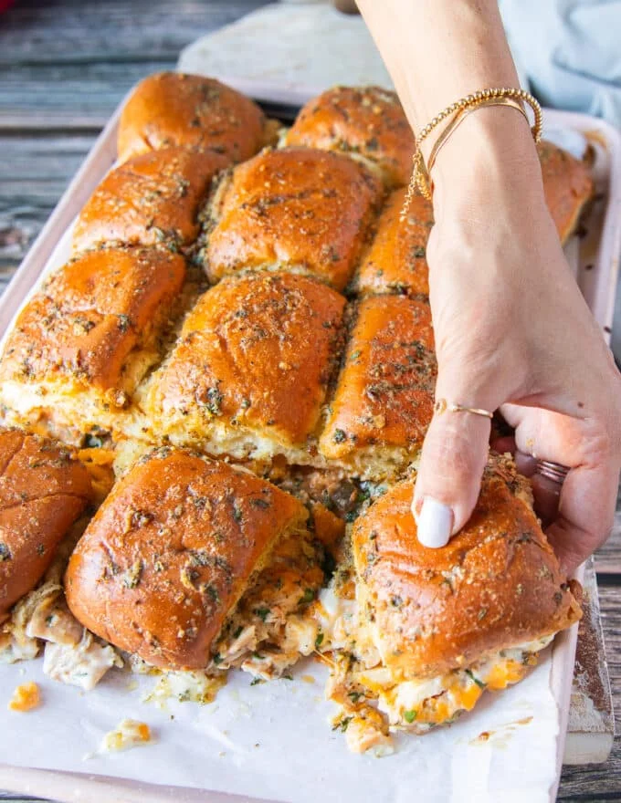 A hand pulling away one chicken slider from the sliders pan