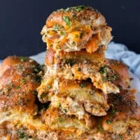 close up of a tower of 4 stacked chicken sliders with cheese oozing out and soft bread