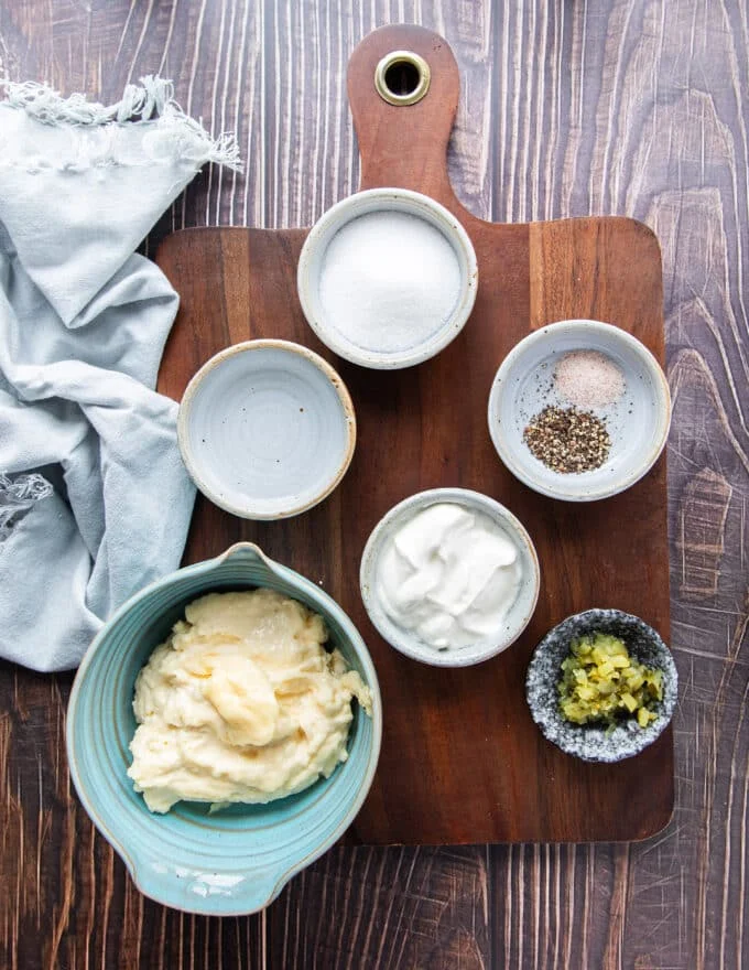 small bowls of separate ingredients needed to make coleslaw dressing over a wooden board.