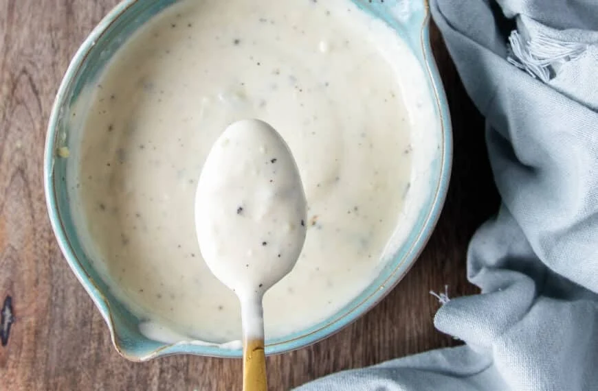 A spoon showing close up texture of coleslaw dressing over a bowl of dressing