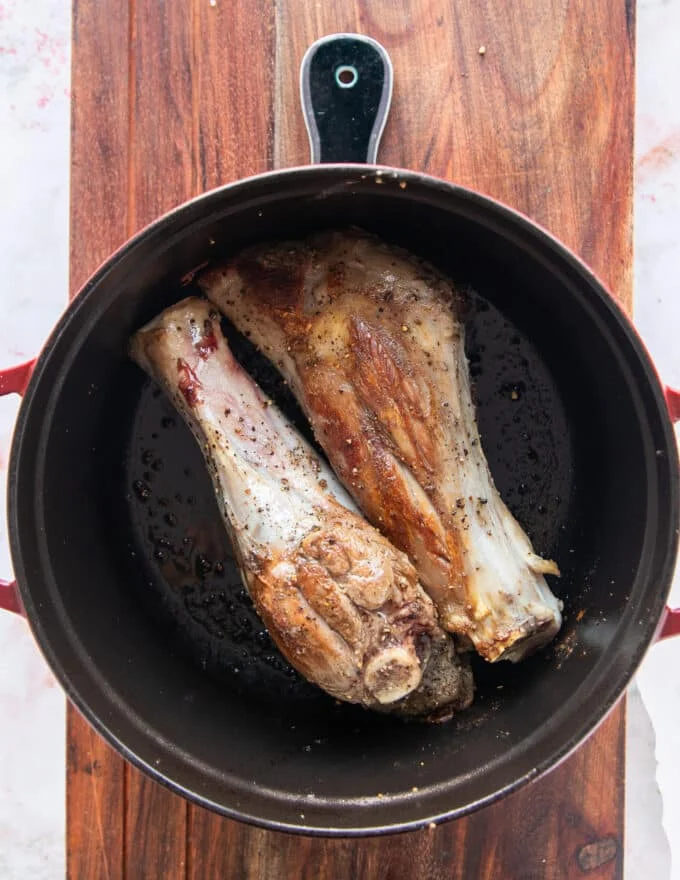 flipped and golden brown lamb shanks in the dutch oven