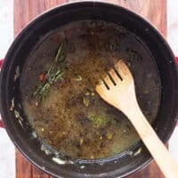 stock, tomatoes, herbs are added to the dutch oven to create the liquid for slow cooking lamb shanks