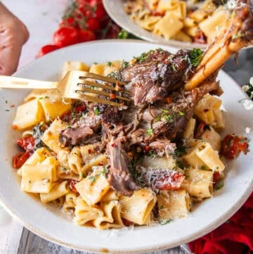 A fork breaking apart a slow cooked lamb shank over pasta showing how fall of the bone it is
