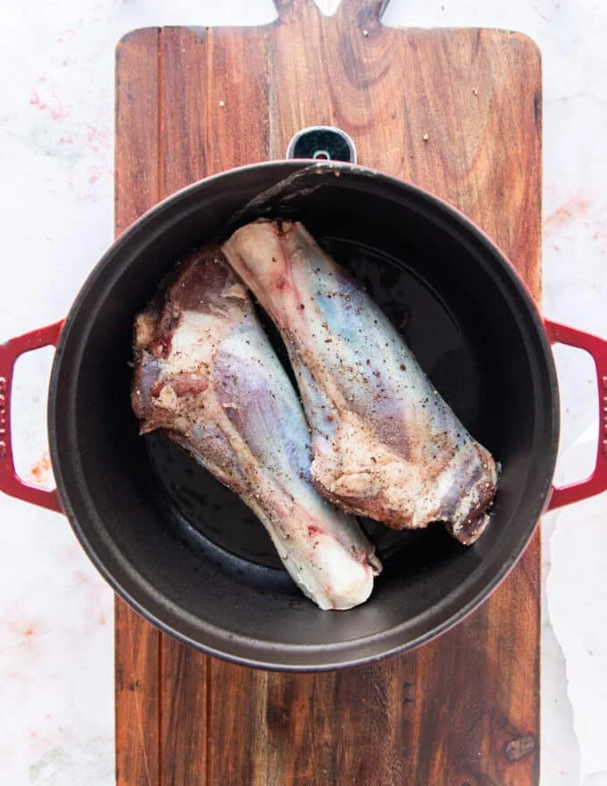 seasoned lamb shanks searing in a Dutch oven over high heat