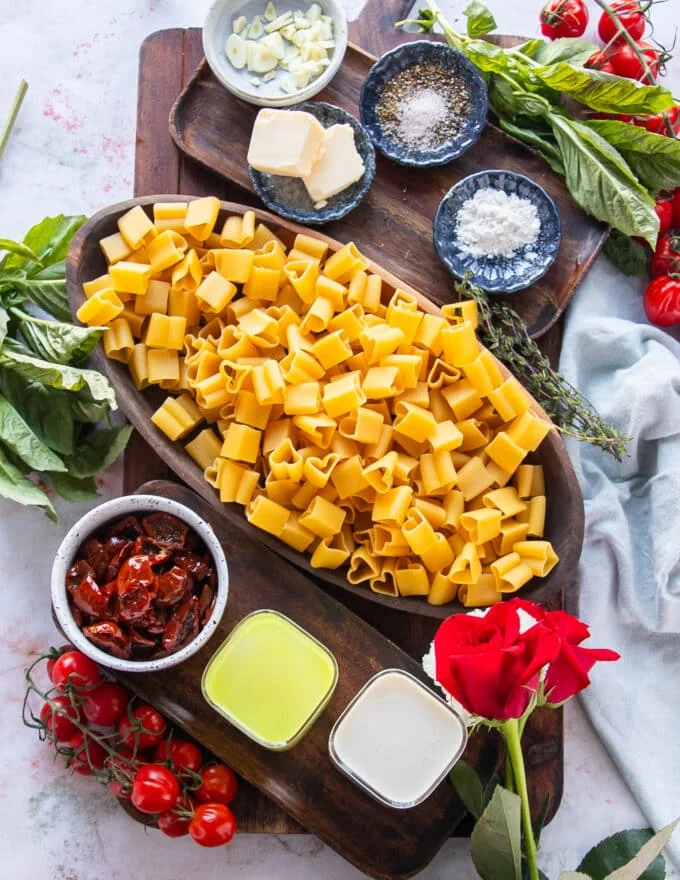 The simple ingredients needed to make sun dried tomato pasta on aboard in small bowls