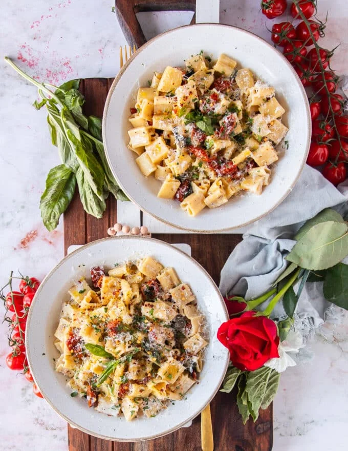 two bowls of sun dried tomato pasta served with lots of parmesan cheese for garnish and fresh basil
