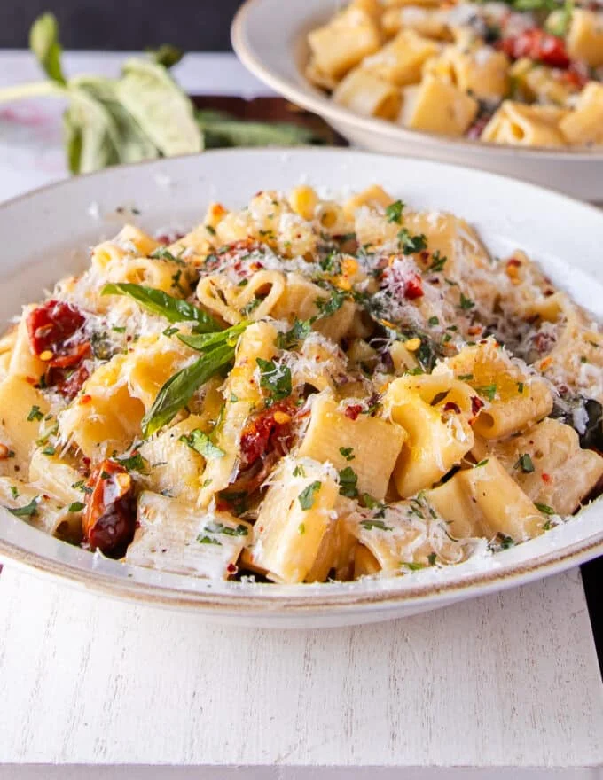 sun dried tomato pasta on a plate with lots of fresh parmesan and basil to garnish