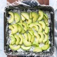the fist layer of filling of the sushi cake is avocado so a thinly sliced layer of avocado is arranged over the rice