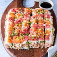 inverted and decorated sushi cake that's cut into small pieces so it's easy to eat and grab garnished with green onions and furikake