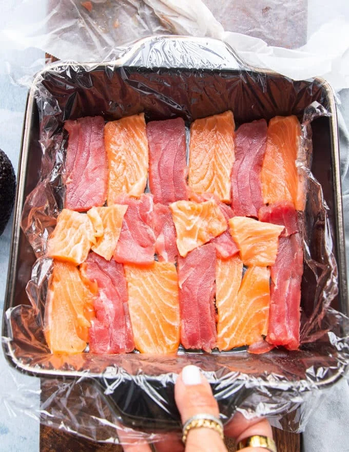 A ray os thinly sliced ahi tuna and sushi grade salmon are arranged a the bottom of the dish to make the fist layer of the cake when flipped.