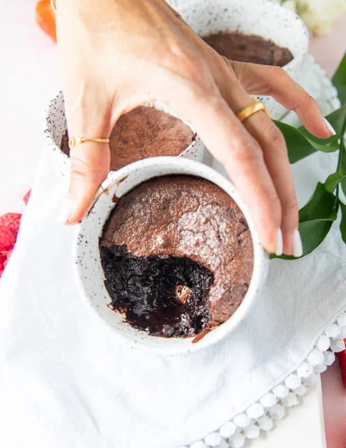 a hand holding a dish of brownie pudding close up showing the contrast in texture with the crackly tops and insides very soft and molten