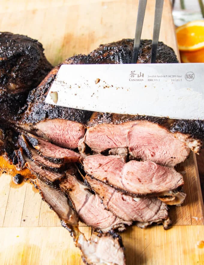 A sharp knife slicing a butterflied leg of lamb showing the perfectly cooked lamb