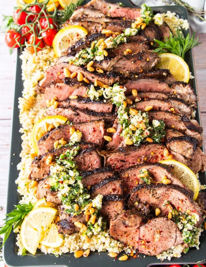 A platter of sliced butterflied leg of lamb on a bed of herbs