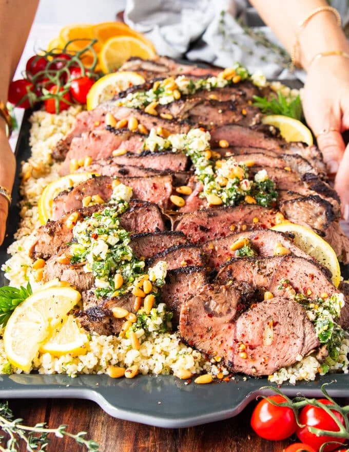 A hand holding a huge platter of sliced butterflied leg of lamb