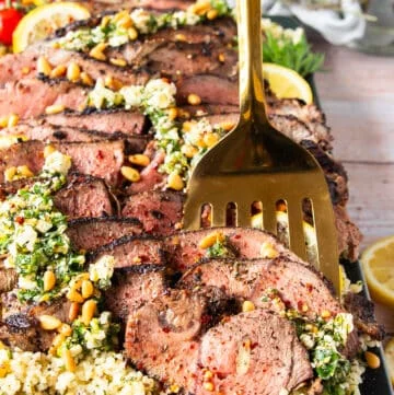 A spoon holding up a slice of butterflied leg of lamb close up showing the perfectly cooked butterflied leg of lamb