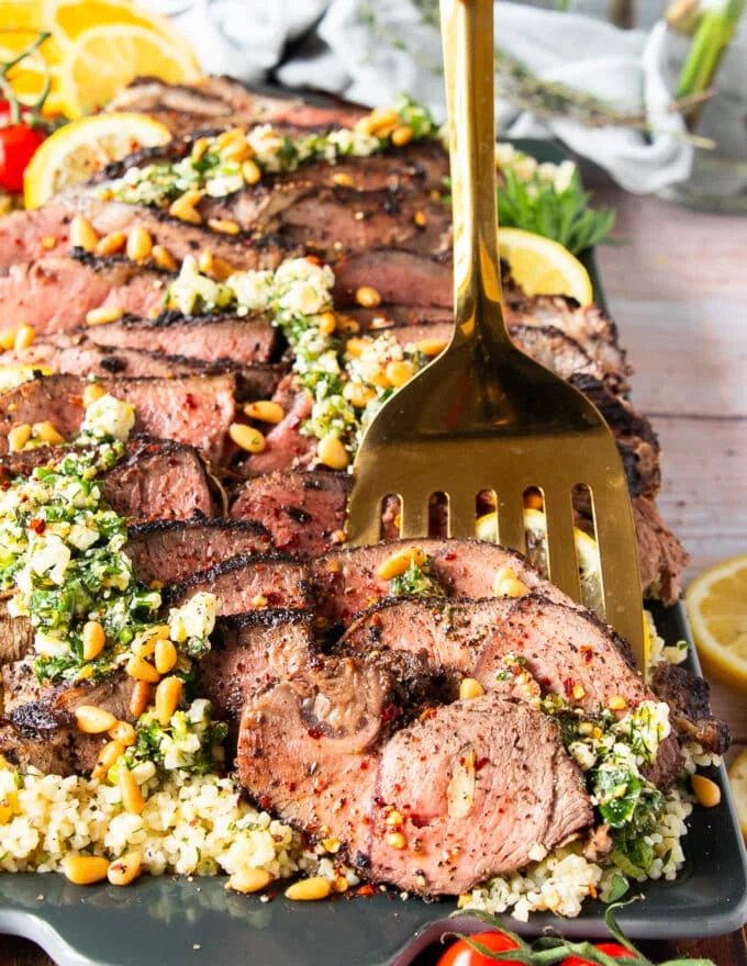A spoon holding up a slice of butterflied leg of lamb close up showing the perfectly cooked butterflied leg of lamb