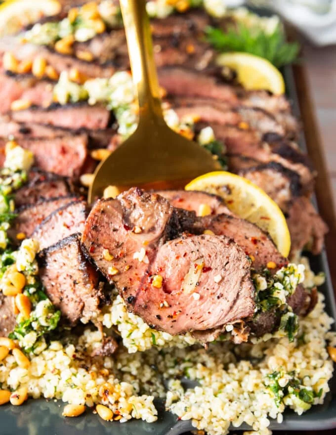 close up of a serving of butterflied leg of lamb on a slotted spoon showing the texture close up