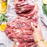 garlic slices being inserted along the leg of lamb to infuse with flavor