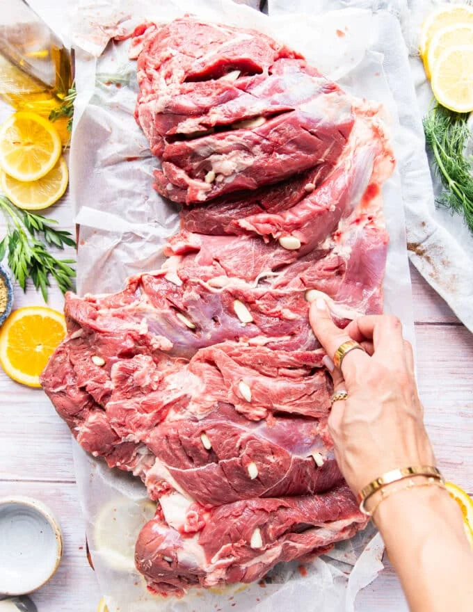 garlic slices being inserted along the leg of lamb to infuse with flavor