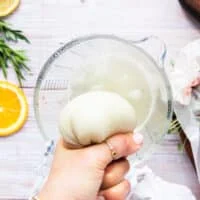 A hand squeezing the water out of the grated onion in the kitchen towel