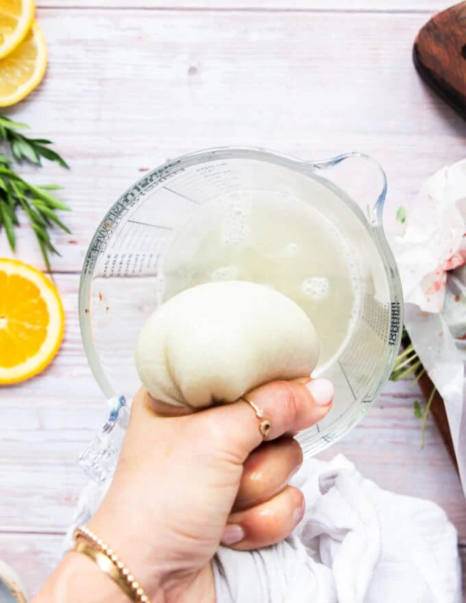A hand squeezing the water out of the grated onion in the kitchen towel