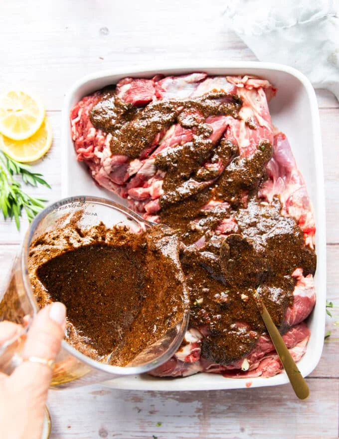the lamb marinade being poured over the lamb in a shallow dish