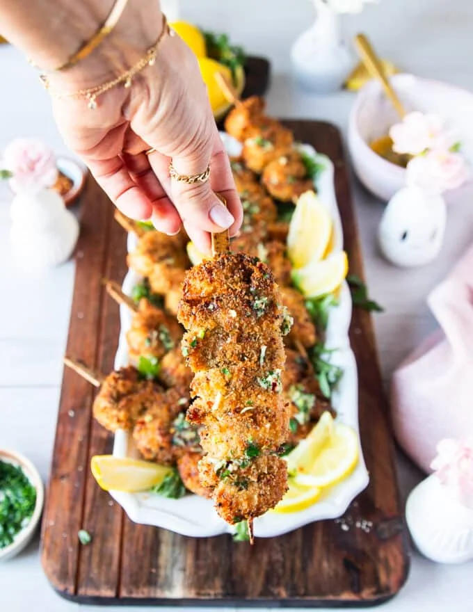 A hand holding a skewer of crisp golden chicken spiedini skewer drizzled with melted garlic lemon herb butter