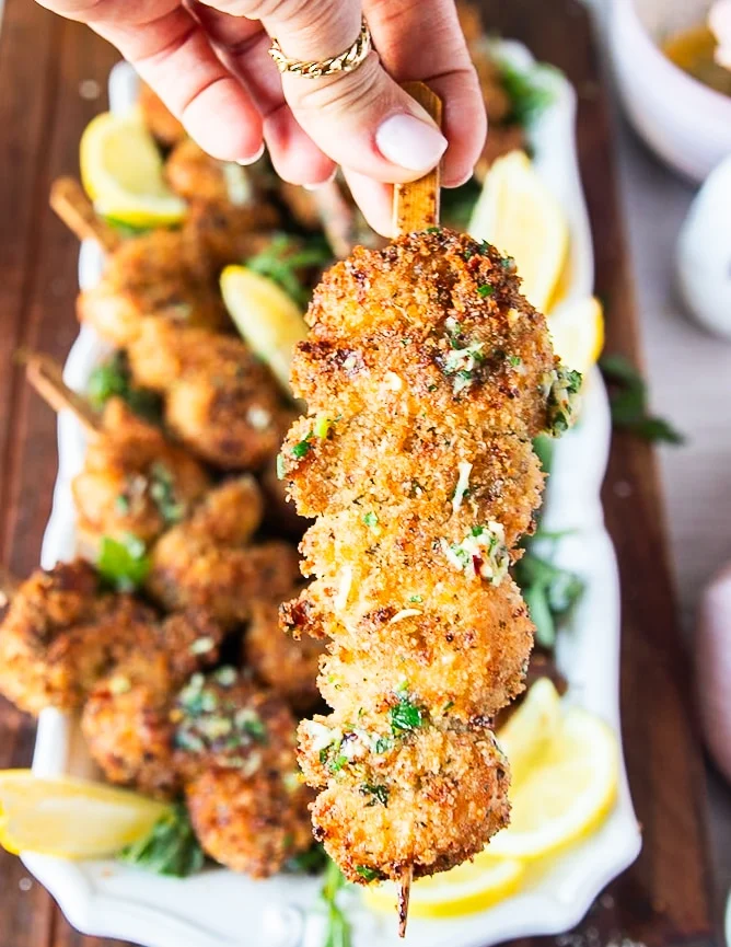 A hand holding one chicken spiedini close up showing the crunchy chicken and lemony butter drizzle on a skewer