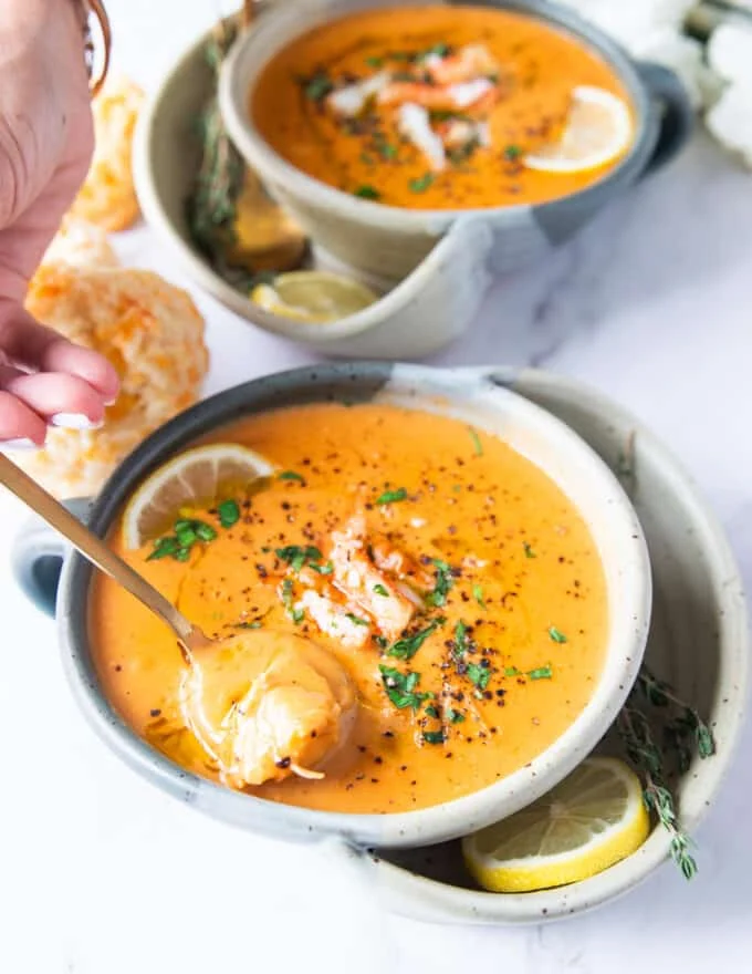 A spoon spooning up some crab bisque showing how silky it is and the lumps of crab meat