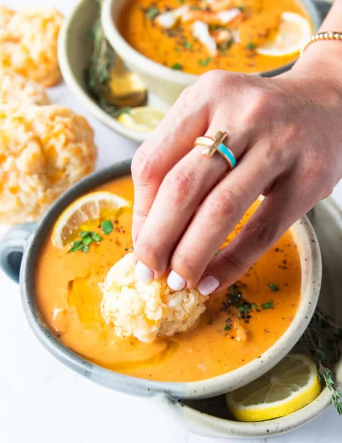 A hand dipping in some buttery drop biscuits into the crab bisque