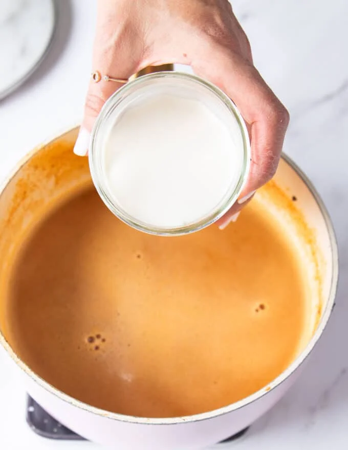 A hand adding cream to a blended soup