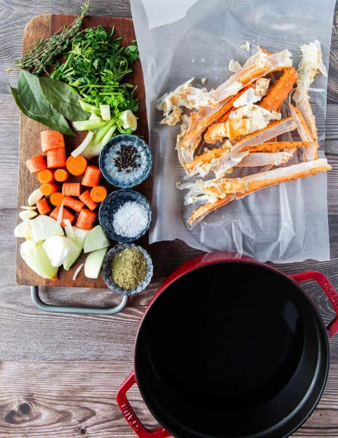 A large board of ingredients to make crab stock including crab shells, water, some carrots, celery, bay leaves whole peppercorn, garlic and more , all in small bowls
